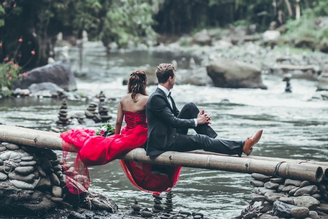 Couple in love sitting on the bench by the water. Woman in red, man in grey